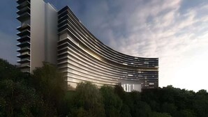 A modern, curved building with multiple balconies, surrounded by greenery.