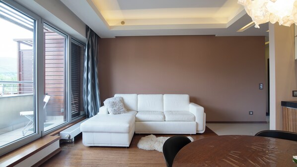 Una sala de estar moderna con un sofá blanco, un pequeño reposapiés y una mesa de comedor de madera.