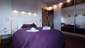 Une chambre à coucher moderne avec un grand lit, une table de chevet, un miroir et une porte.