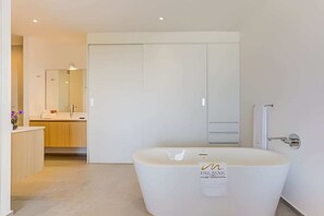 Une salle de bain moderne avec une baignoire sur pieds, un grand miroir et un dressing.