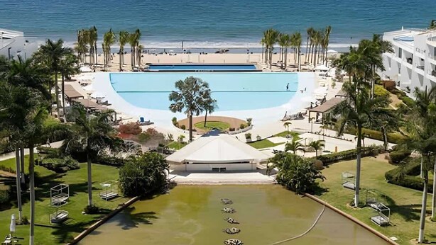A resort with a large swimming pool, a tennis court, and a beach view.