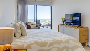 A hotel room with a large bed, a TV on a wooden cabinet, a balcony with a view, and a window with curtains.