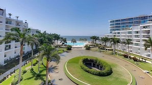 A modern hotel with multiple floors, a swimming pool, and palm trees.