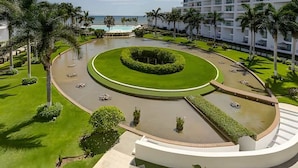 A hotel with a circular pool, palm trees, and a view of the ocean.