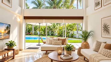 A spacious living room with a large window, a ceiling fan, and a view of a swimming pool and tropical garden.