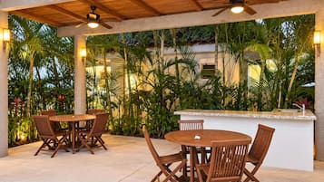 An outdoor patio area with wooden tables and chairs, a ceiling fan, and a bar counter.
