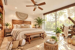 A bedroom with a wooden headboard, a large bed, a bench, a bedside table, a floor lamp, and a view of palm trees through a large window. - Beach Days & Poolside Vibes (Bucerías)
