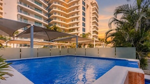 Ein Schwimmbecken mit klarer, blauer Wasseroberfläche, umgeben von einer weißen Poolterrasse und einer weißen Markise.