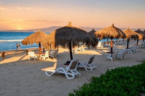 A beach with thatched umbrellas, white lounge chairs, and a view of the ocean. - Pool & Beachfront Stay at Nuevo Vallarta (Bucerías)