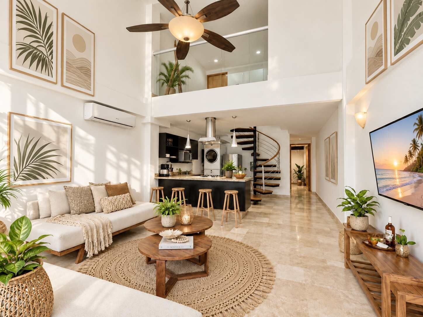 A spacious living area with a sofa, coffee table, and a dining area with stools. A kitchen is visible in the background, and there is a staircase leading to an upper level.