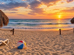 Ein Strand mit einem Seilzaun, einem Strandball und einem Reetdachschirm.