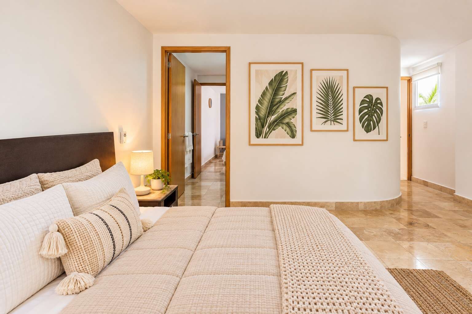 A bedroom with a large bed, a nightstand with a lamp, and a view of a hallway with a door leading to another room.