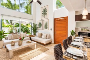 A modern living room with a sofa, coffee table, and dining area with chairs and a table set for a meal. - Coastal Comfort in Nuevo Vallarta (Bucerías)