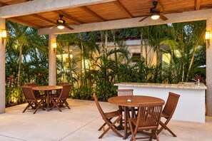 An outdoor patio area with wooden tables and chairs, a ceiling fan, and a bar counter. - Coastal Comfort in Nuevo Vallarta (Bucerías)