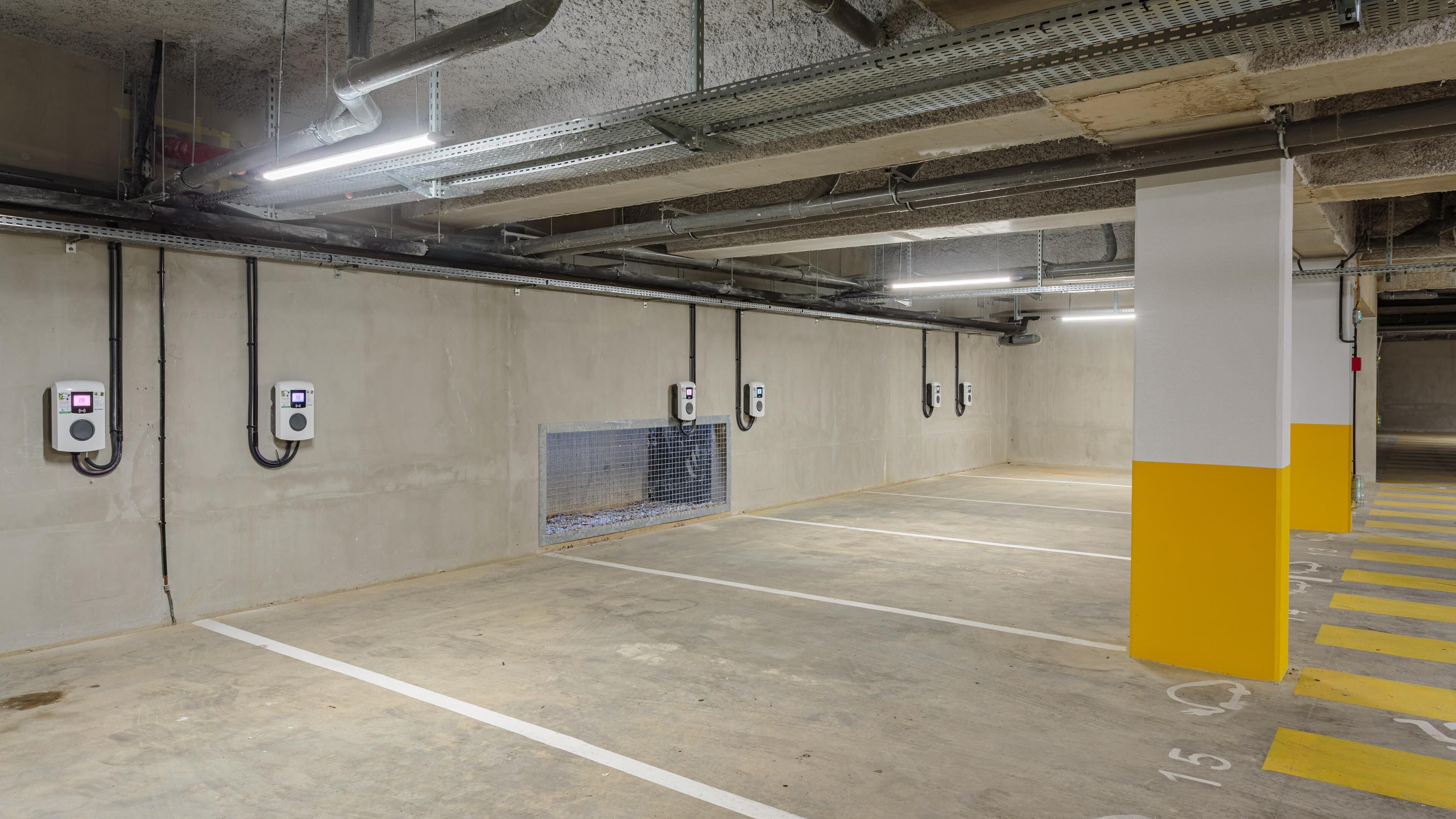 An empty parking garage with concrete walls, fluorescent lighting, and electric vehicle charging stations.