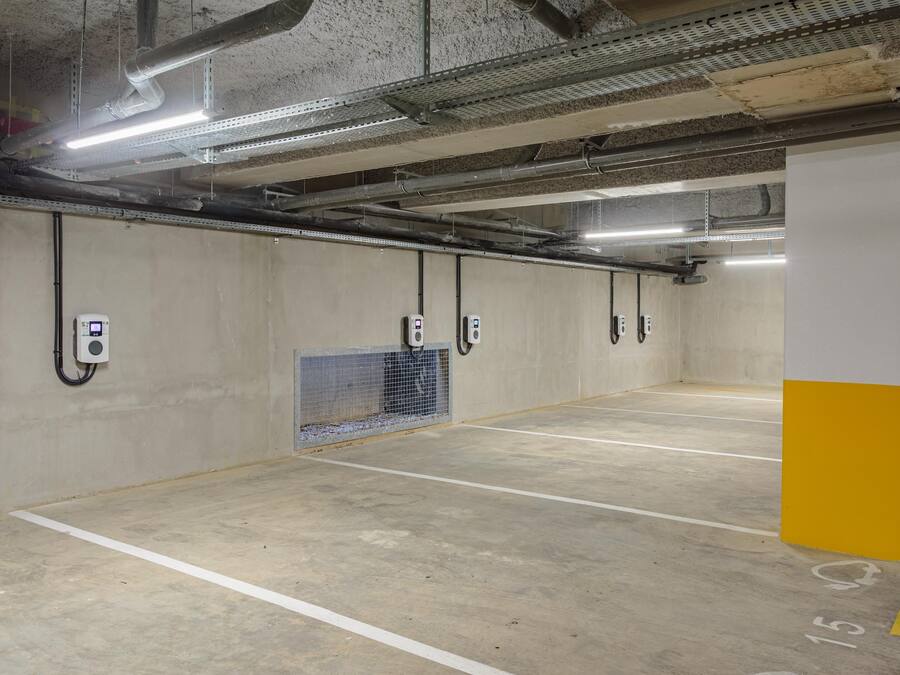 Un estacionamiento vacío con paredes de hormigón, iluminación fluorescente y estaciones de carga para vehículos eléctricos.