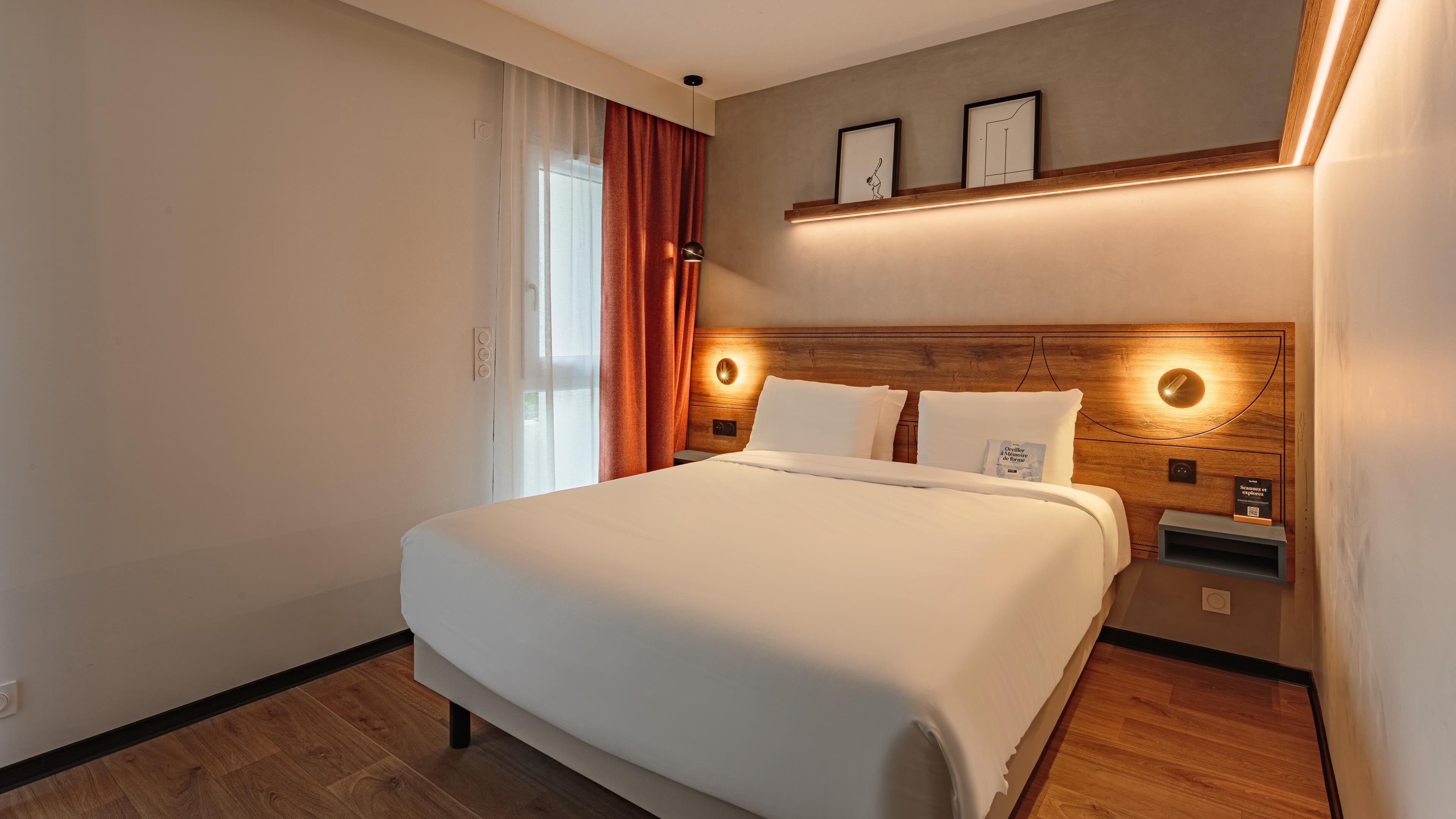 A modern hotel room with a large bed, wooden headboard, and bedside tables.