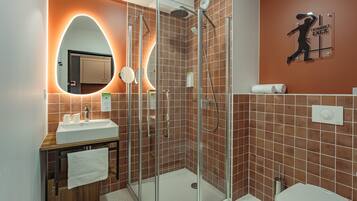 Un baño moderno con ducha de vidrio, un lavamanos con espejo y un inodoro.