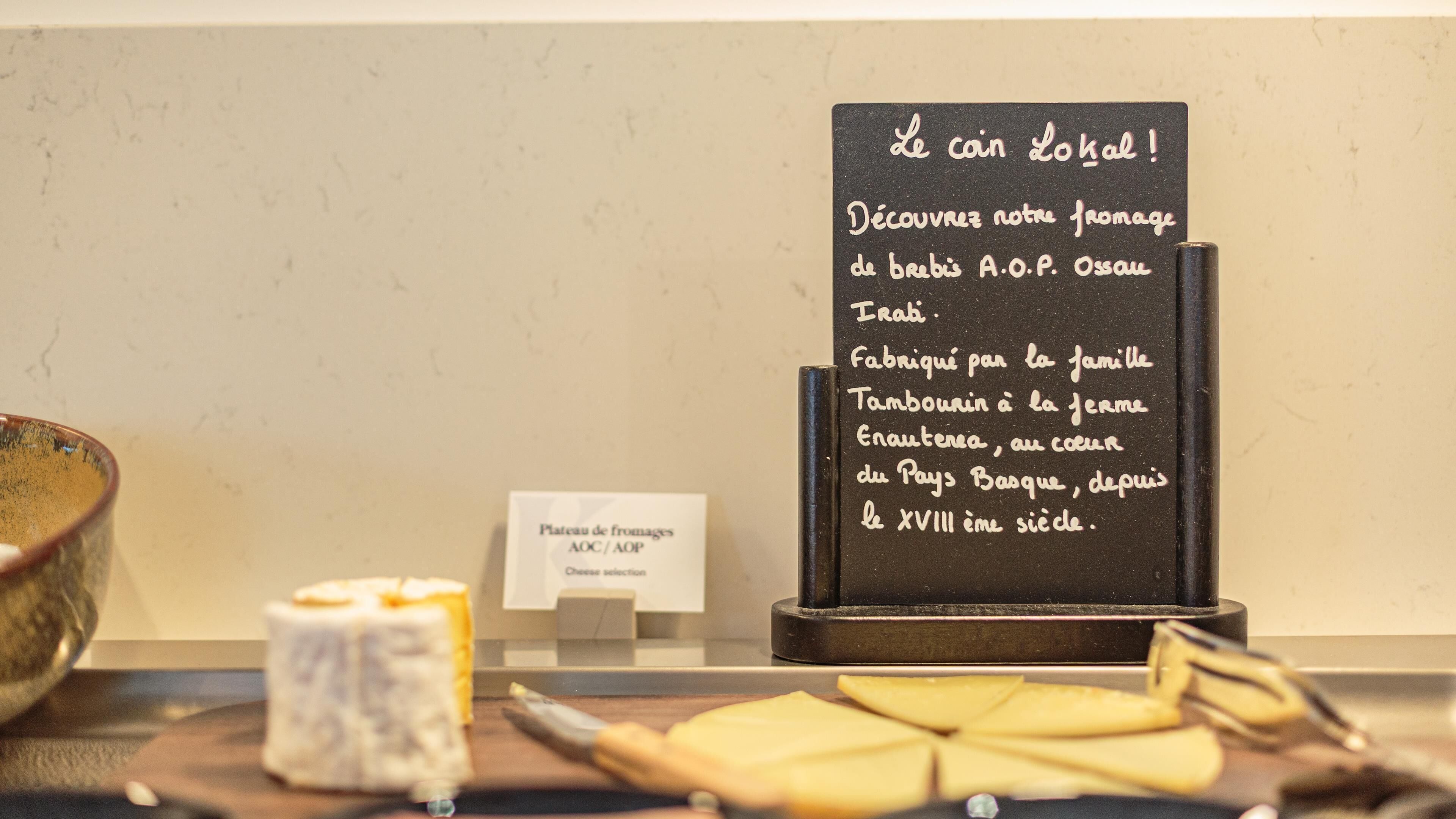 A cheese display with a sign in French, a small sign indicating cheese selection, and a wooden board with cheese slices.