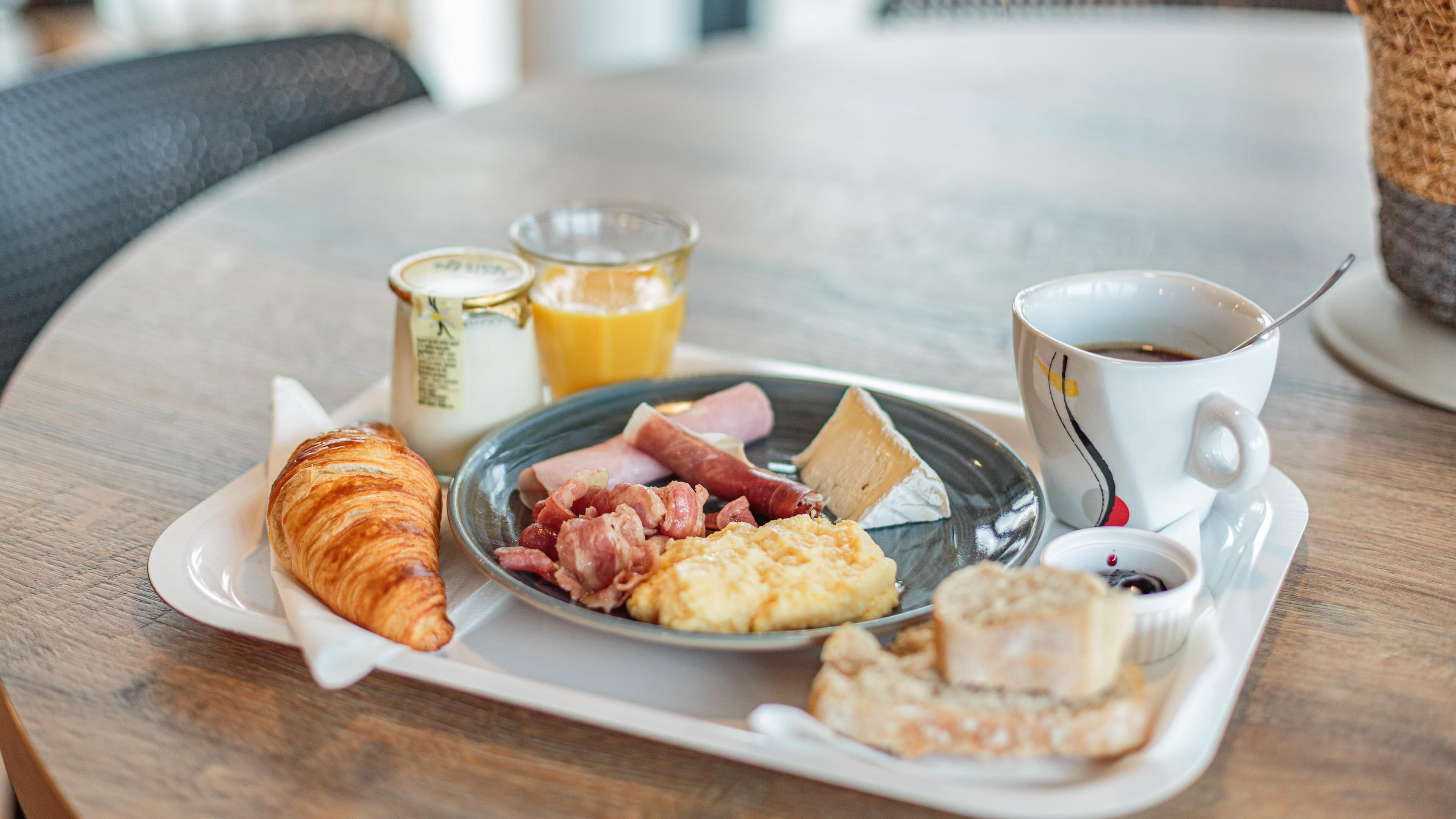 Een ontbijtkarretje met croissant, ham, roerei, kaas en een kop koffie op een houten tafel.