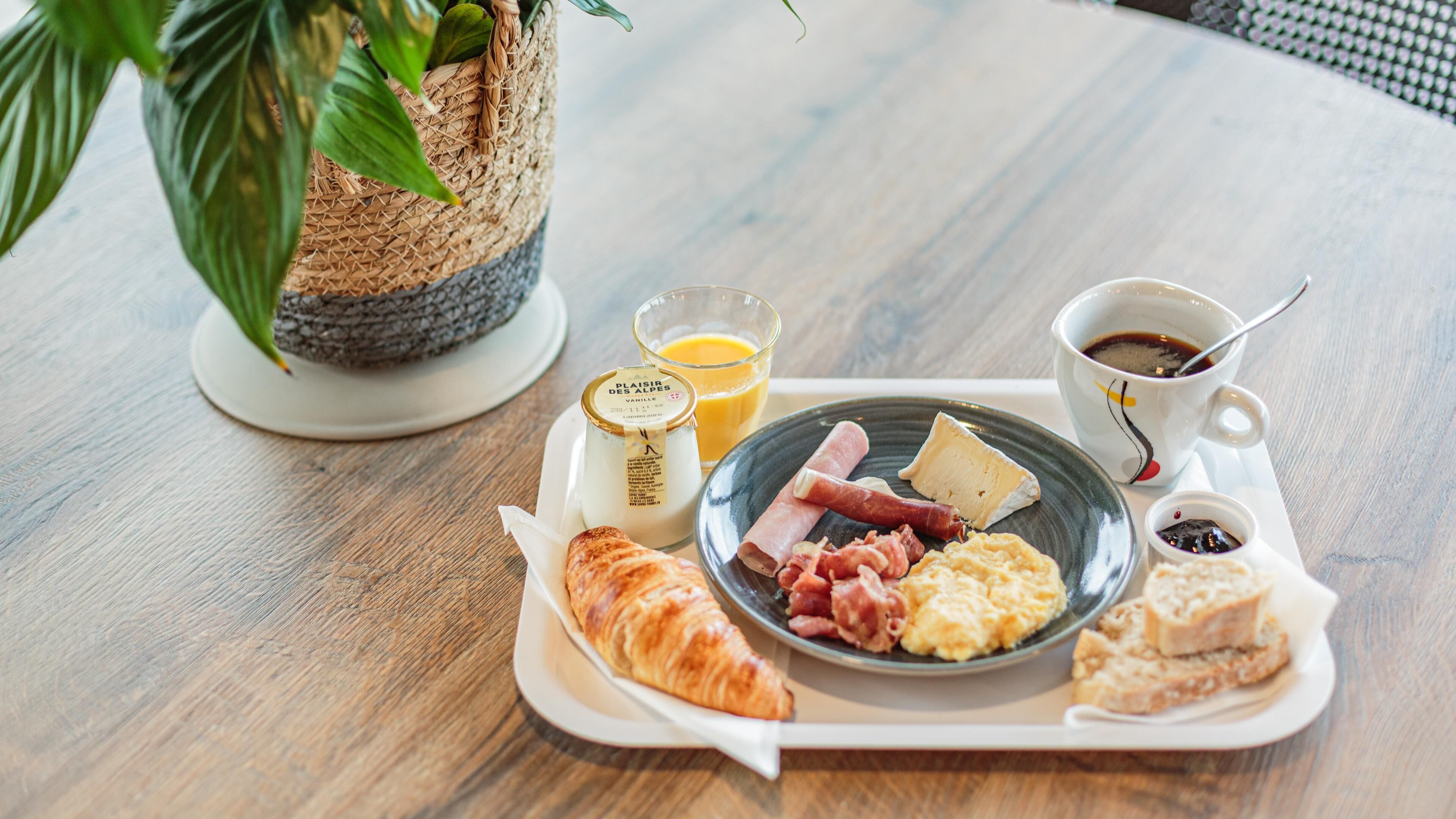A breakfast tray with croissants, scrambled eggs, ham, cheese, and a cup of coffee on a wooden table.