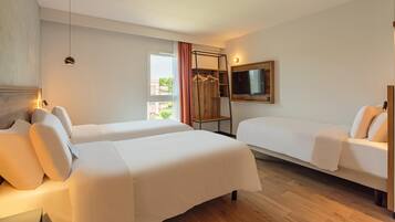 A hotel room with two beds, a TV mounted on the wall, a wooden floor, and a window with curtains.