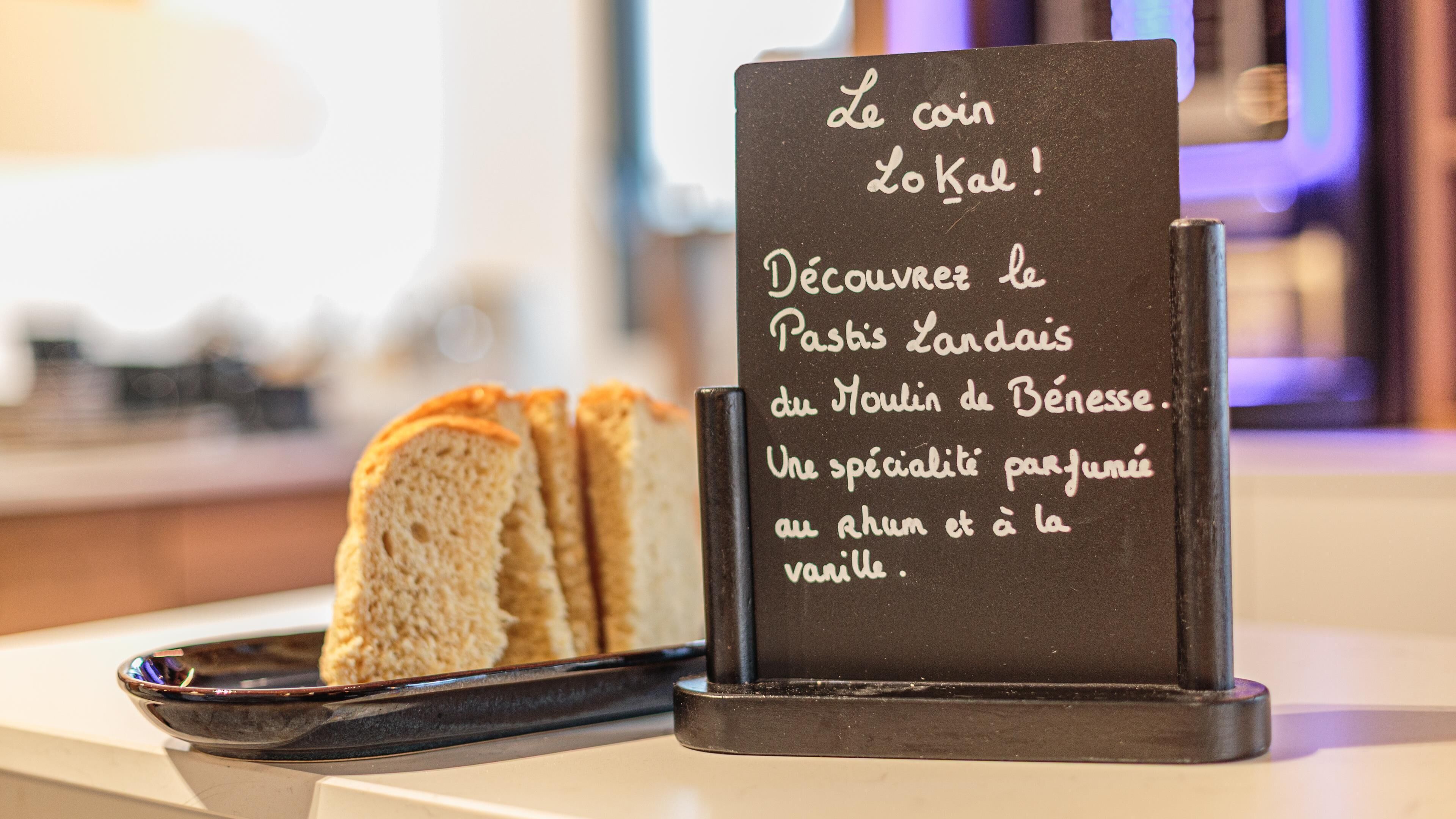 A sign with French text describing a specialty pastry, accompanied by a tray of sliced bread.
