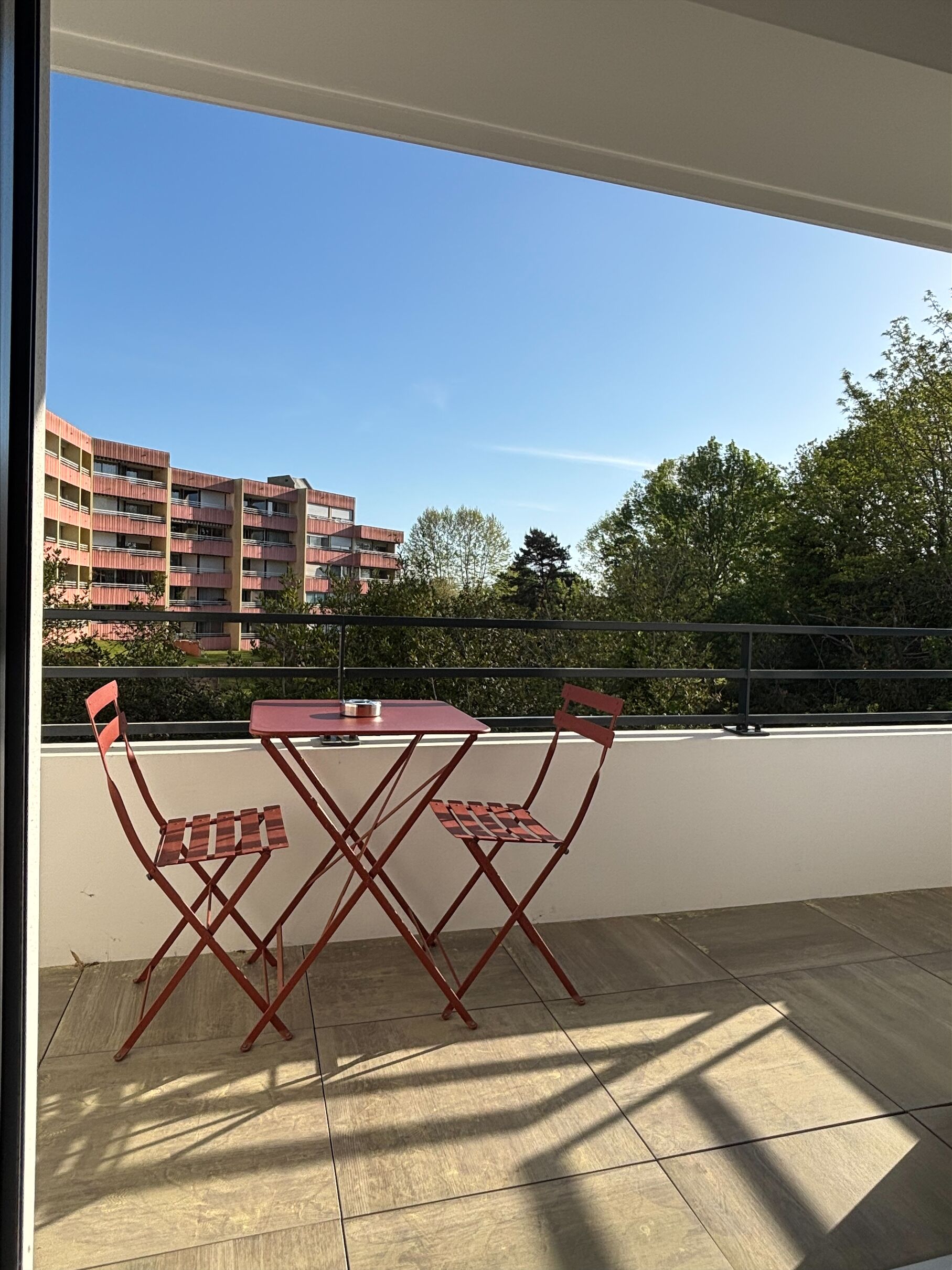 Een balkon met een tafel en stoelen, uitzicht op gebouwen en een heldere lucht.