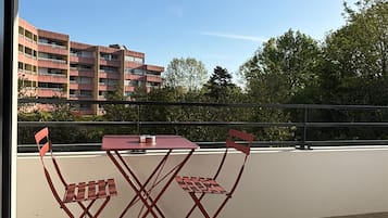 Een balkon met een tafel en stoelen, uitzicht op gebouwen en een heldere lucht.