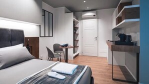 Une chambre d’hôtel moderne équipée d’un lit, d’un bureau, d’une chaise, d’une petite table et d’étagères intégrées.