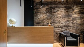 Un espace d’accueil comprenant un comptoir de réception en bois, un canapé noir agrémenté d’un coussin à motifs et un mur en pierre.
