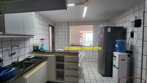 A compact kitchen with white tiled walls, a black countertop, a stainless steel sink, a water dispenser, and a black refrigerator. - Best 3-suite apartment with beach view by the sea, swimming pools and excellent facilities (Pirangi do Norte Parnamirim)