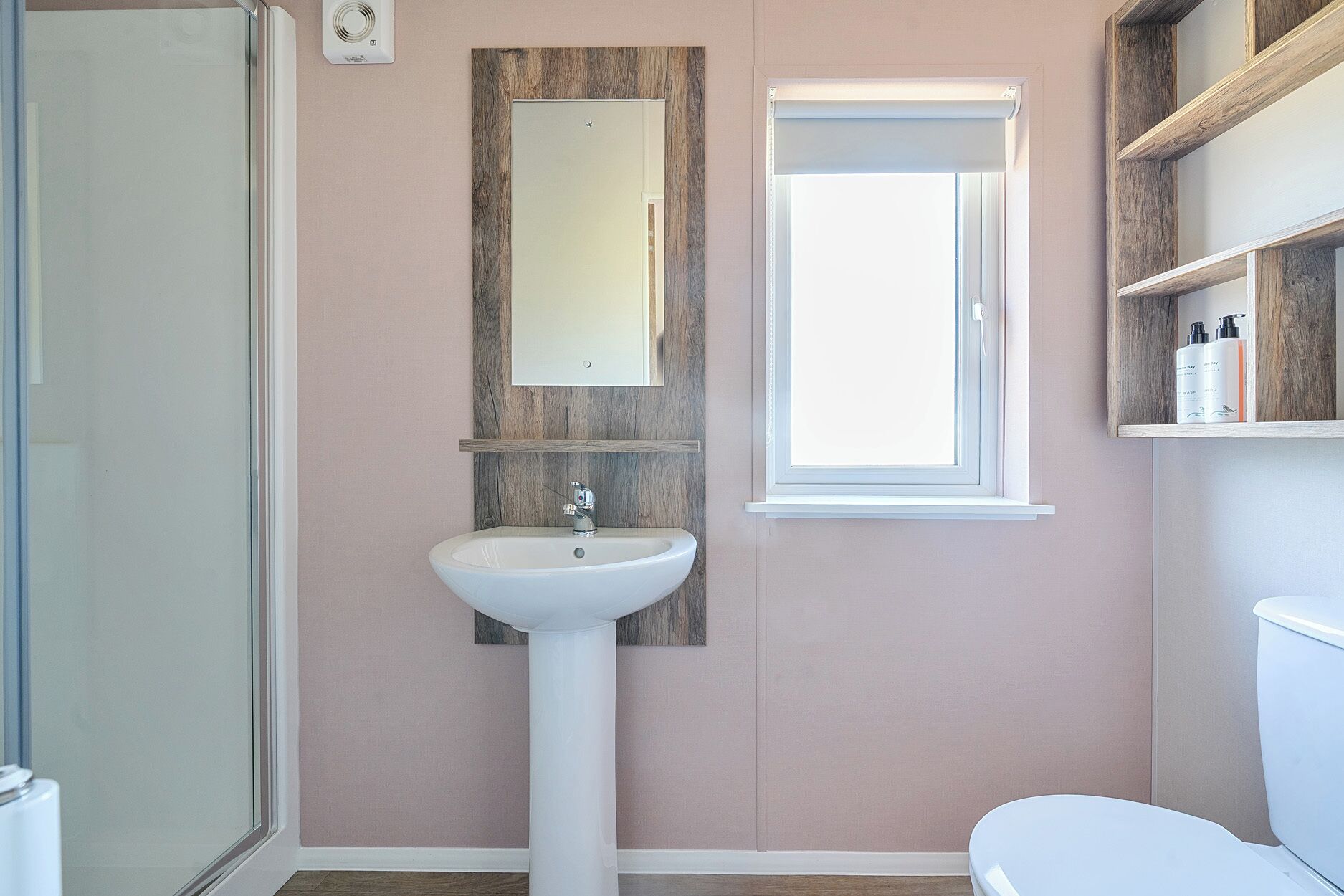 Un baño con un lavamanos blanco, un espejo, un ventanal y una ducha.