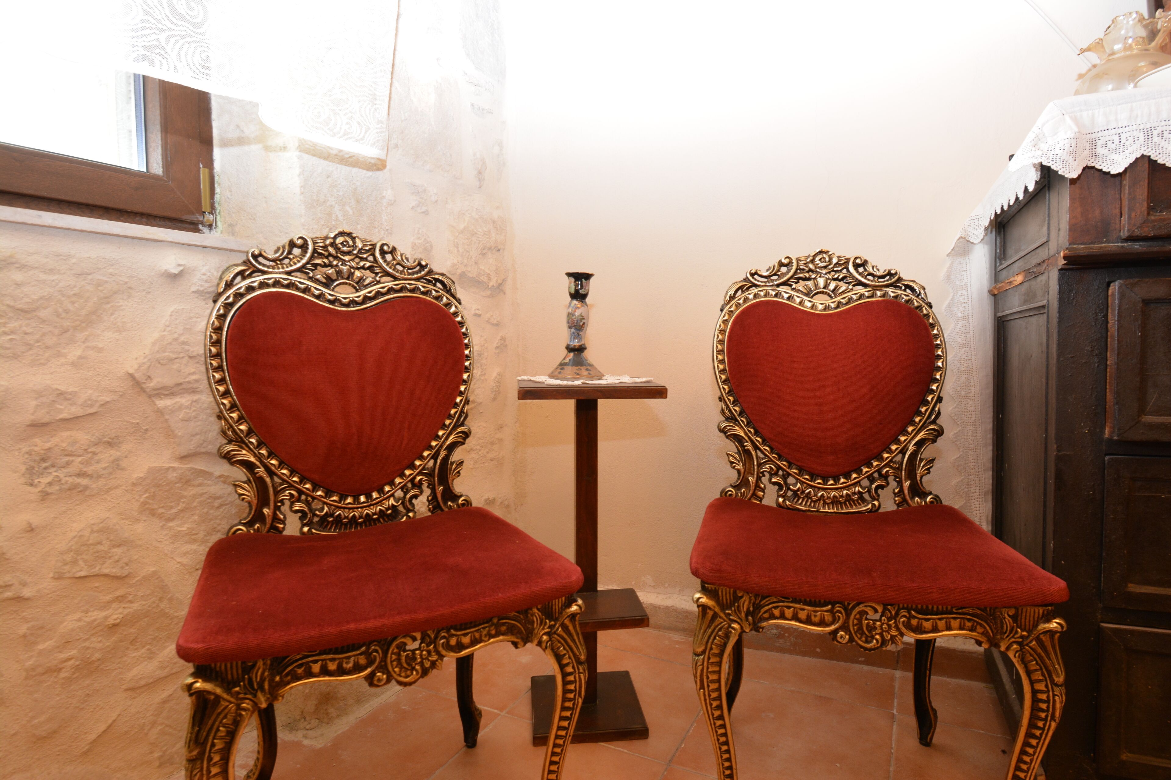 Two ornate chairs with red velvet upholstery and gold detailing, positioned in front of a small table with a candle.
