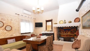 A cozy living room with a wooden dining table, patterned chairs, a sofa, and a fireplace with decorative items. - Gioma Stone House by Checkin (Heraklion)
