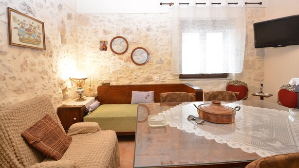 A cozy living room with a sofa, a glass coffee table, a lamp, and a television mounted on the wall. - Gioma Stone House by Checkin (Heraklion)