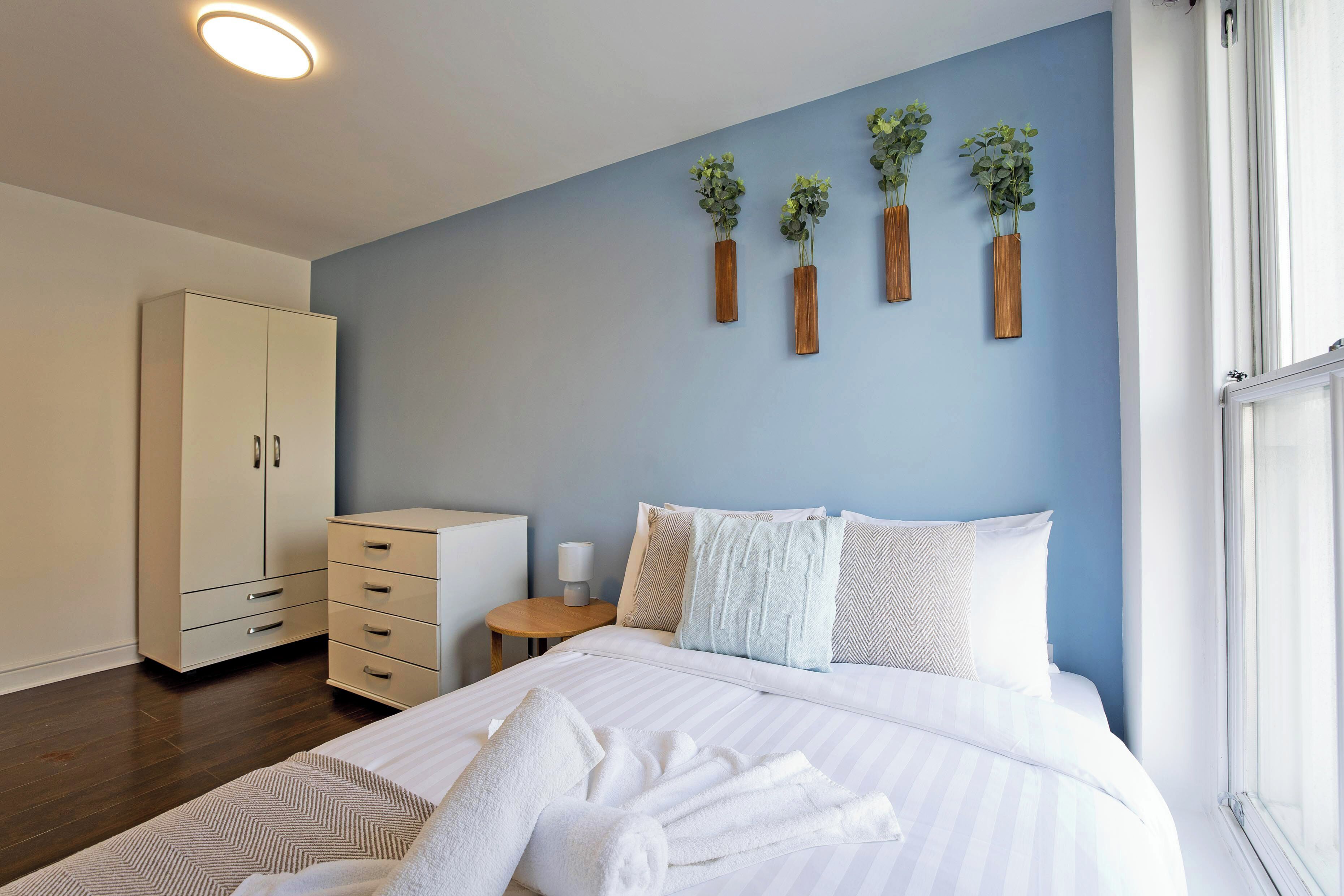 A bedroom with a bed, bedside table, nightstand, wardrobe, and wall-mounted plants.