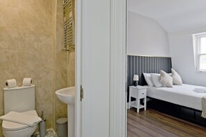 Un bagno con il water, un lavandino e una doccia. La stanza dispone di un letto con biancheria bianca e un comodino con una lampada.