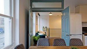 Un coin repas avec une table en bois et quatre chaises, une porte bleue et un réfrigérateur à l’arrière-plan.