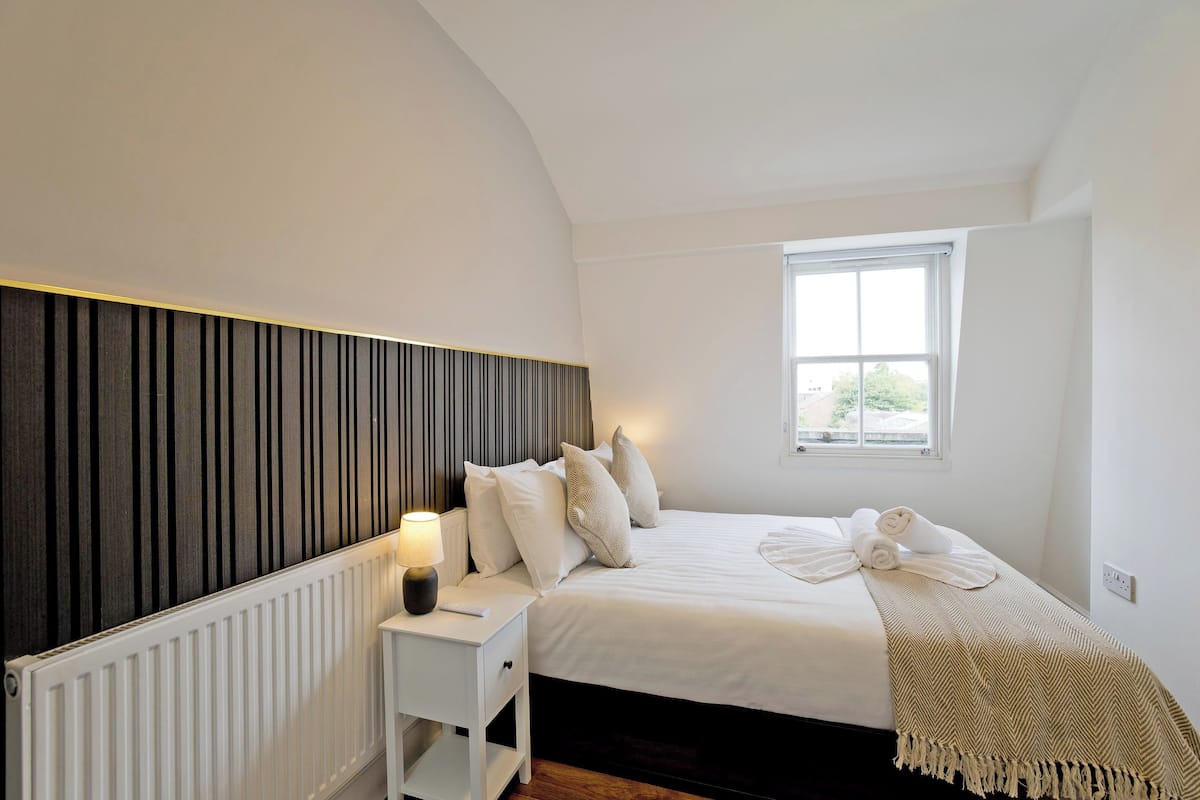 Une chambre à coucher avec un lit, une table de chevet, une lampe et une fenêtre.