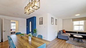 Un salon moderne avec une table à manger en bois, des chaises bleues, un canapé gris et une petite table ronde avec une télécommande.