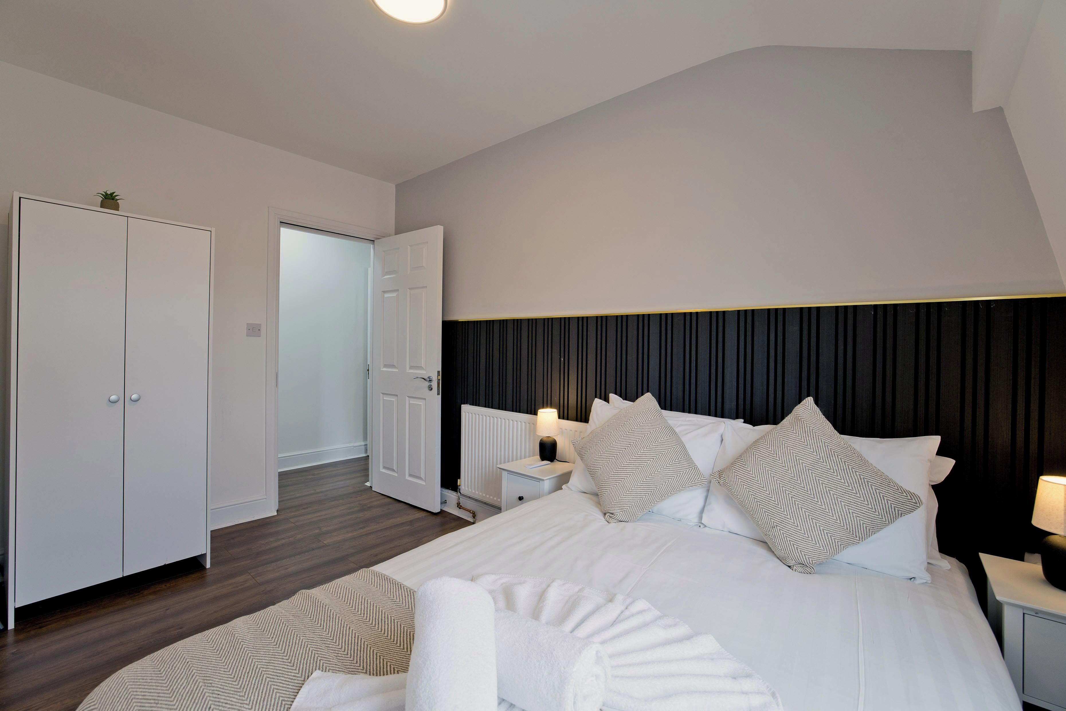 A modern bedroom with a large bed, white wardrobe, and a dark headboard.