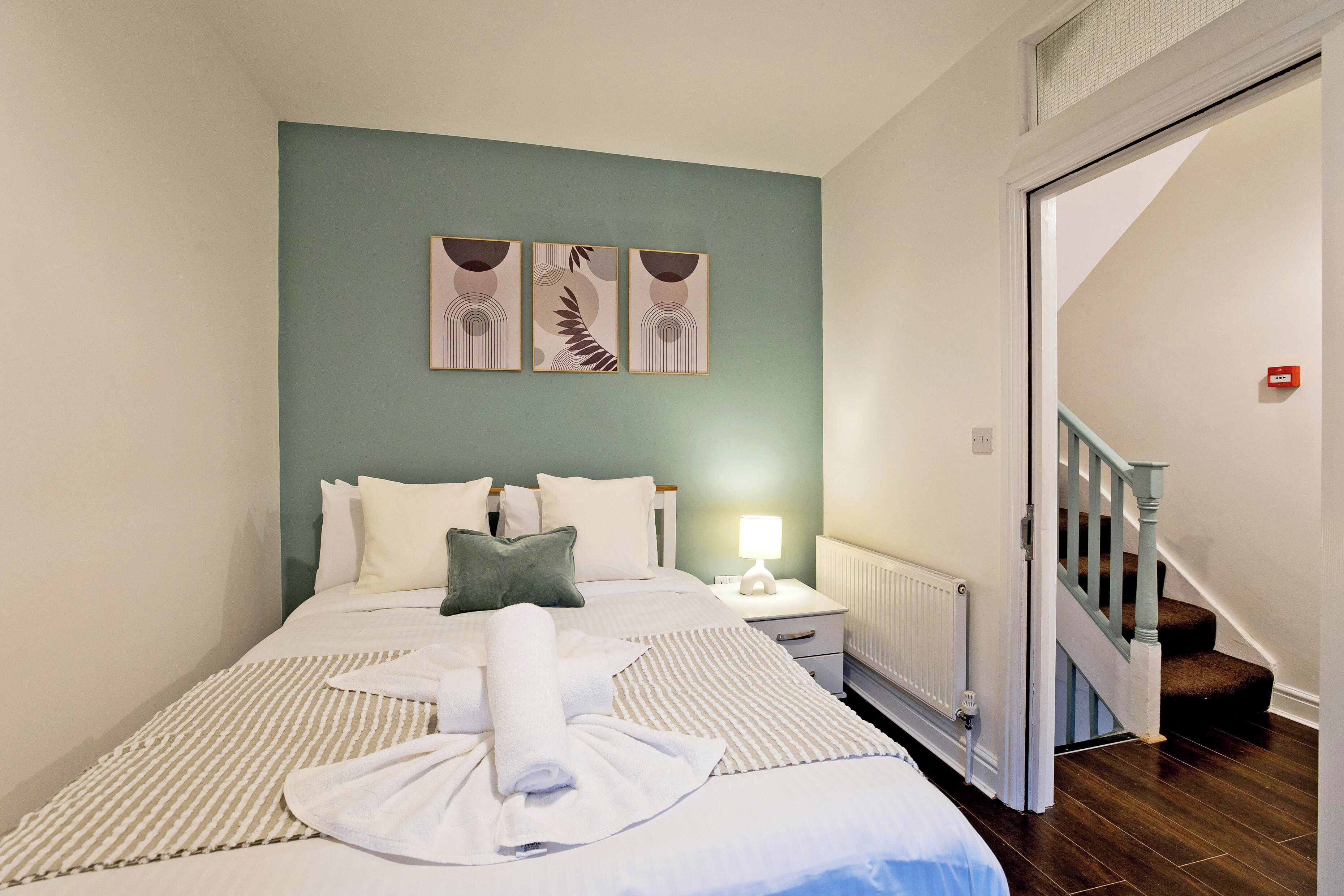 A hotel room with a bed, a nightstand, a lamp, and a view of a staircase.