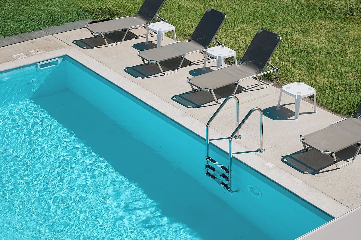 Una piscina con superficie d'acqua cristallina e blu, circondata da lettini e tavolini.