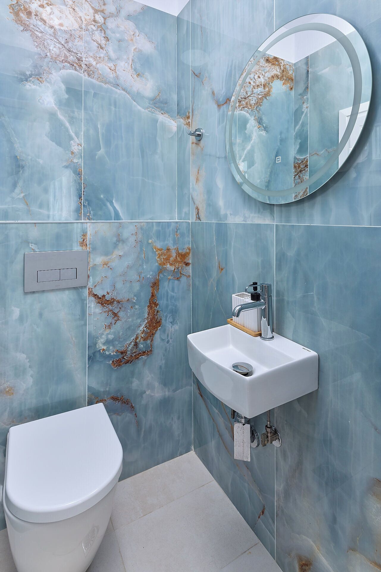A bathroom with a marble wall, a round mirror, a white sink, and a toilet.