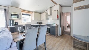A compact kitchen with modern appliances, a dining area with a table and chairs, and a visible bedroom in the background. - Lakeside Lullaby - Billing Aquadrome (Northampton)