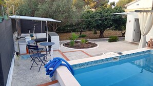 En baghave med swimmingpool, grillområde og en lille have.