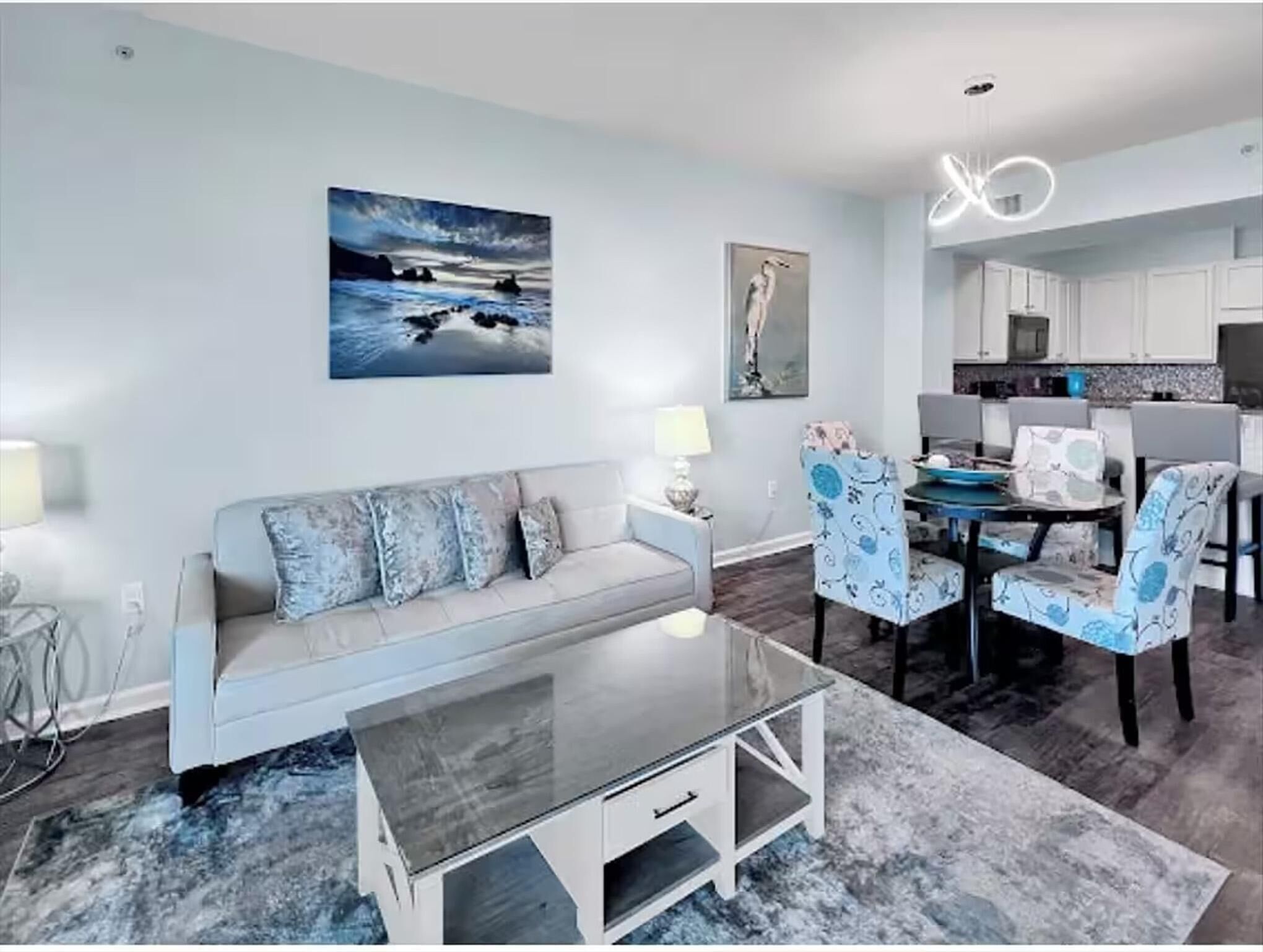 A modern living room with a glass coffee table, a sofa with patterned cushions, and a dining area with patterned chairs.