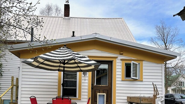 A house with a porch, a red chair, a striped umbrella, and a small table.