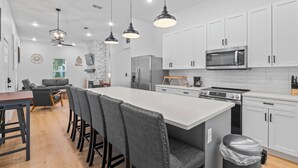 A modern kitchen with white cabinets, a large island, and a dining area with a table and chairs. - Charming Retreat w/ Bikes (Green Cove Springs)